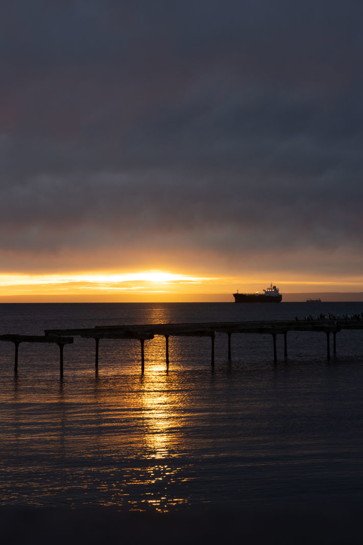 Sunrise over the Strait of Magellan near Punta Arenas, with a cargo ship silhouetted beneath dark clouds