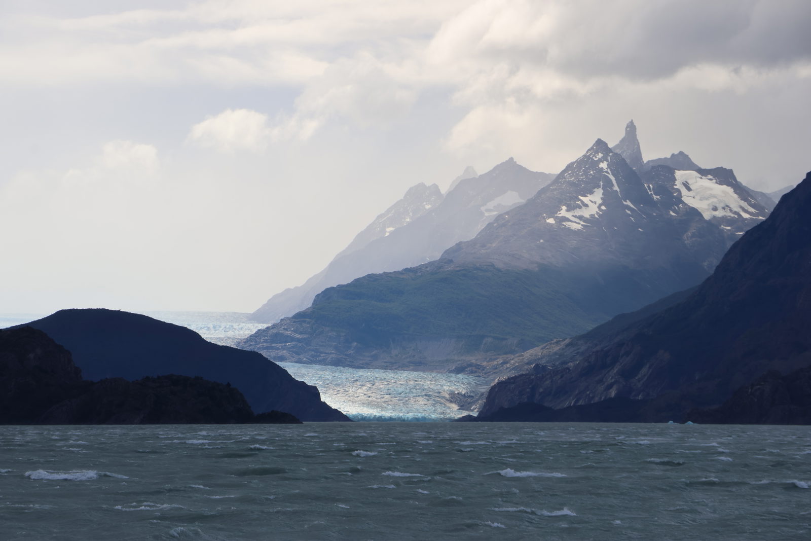 Distant view of Grey Glacier beneath jagged mountain peaks and dramatic skies in Torres del Paine National Park, Chile.