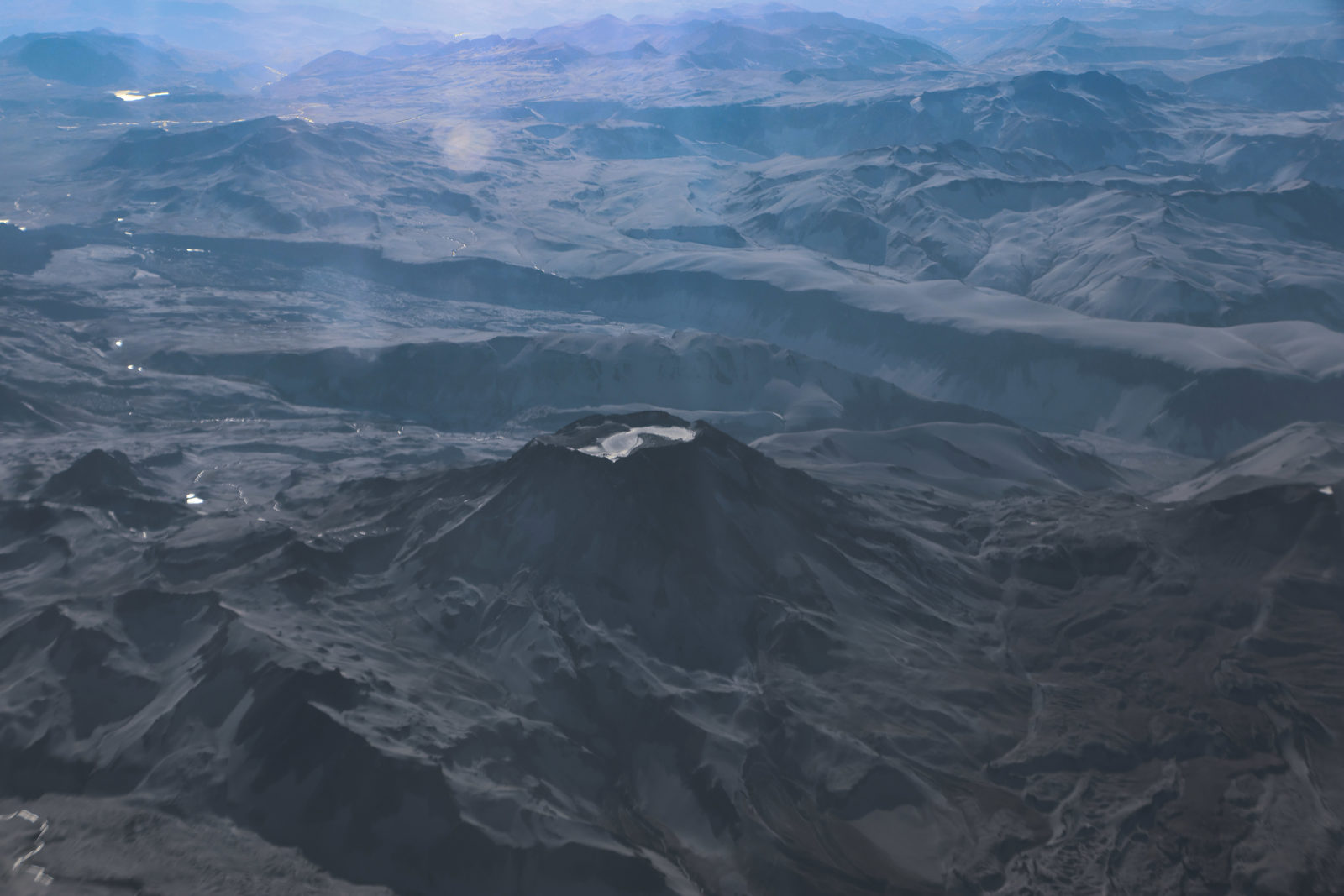 Snow-covered volcanic cone surrounded by rugged Andean landscapes during a flight from Santiago to Punta Arenas in southern Chile.