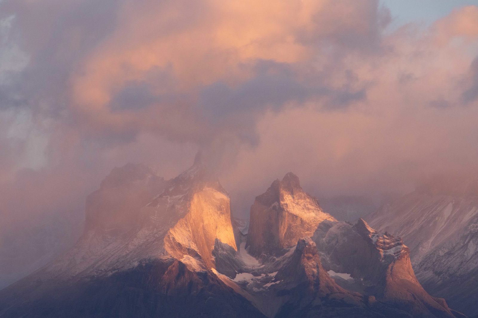 Soft morning light illuminating the Cuernos del Paine peaks beneath swirling clouds in Torres del Paine National Park, Chile.