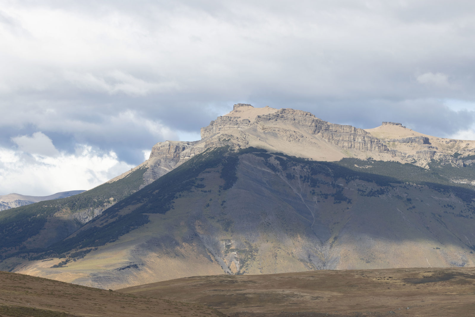 Mountain landscape illuminated by sunlight beneath dramatic clouds in Chilean Patagonia.