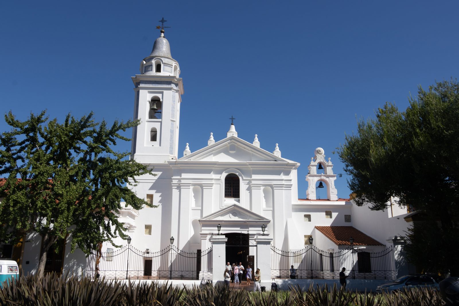White colonial façade and bell tower of the Basilica of Our Lady of Pilar in Recoleta, Buenos Aires, beneath a clear blue sky.