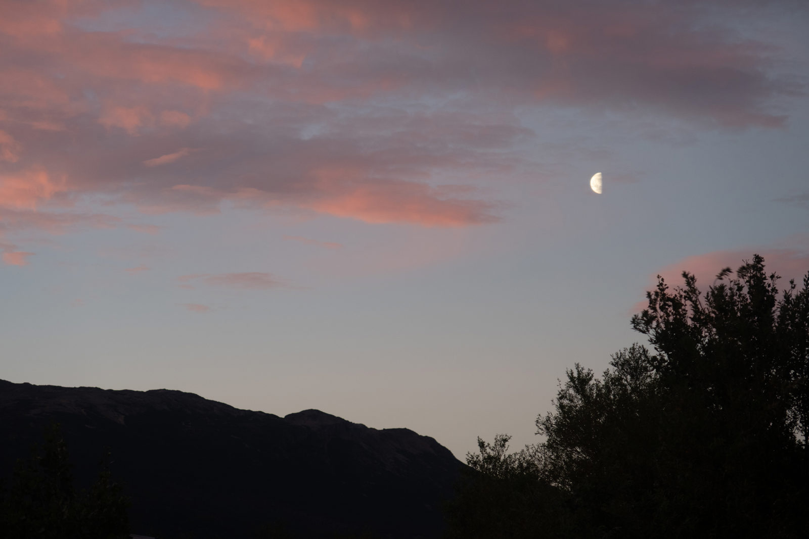 The waxing moon rises above the mountains of El Chaltén beneath pink evening clouds in Patagonia, Argentina.