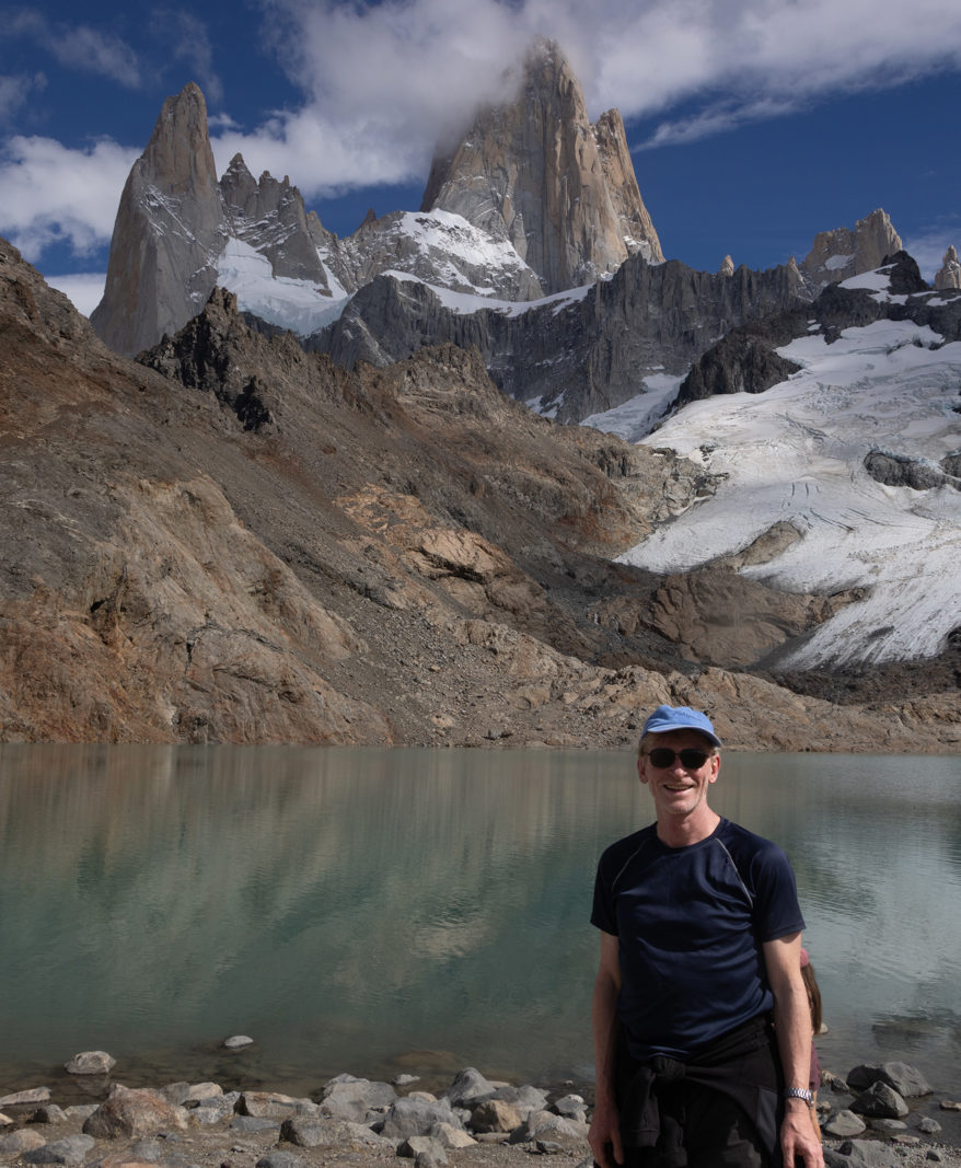 Ian standing beside Laguna de los Tres with Fitz Roy, glaciers and granite spires rising behind the turquoise lake in Patagonia.