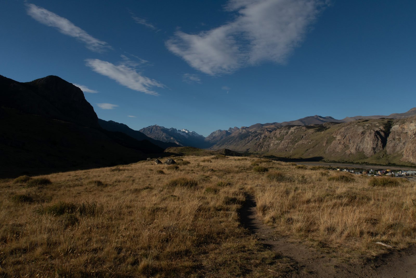 Hiking trail descending towards El Chaltén through golden grassland in the warm evening light beneath the mountains of Patagonia, Argentina.