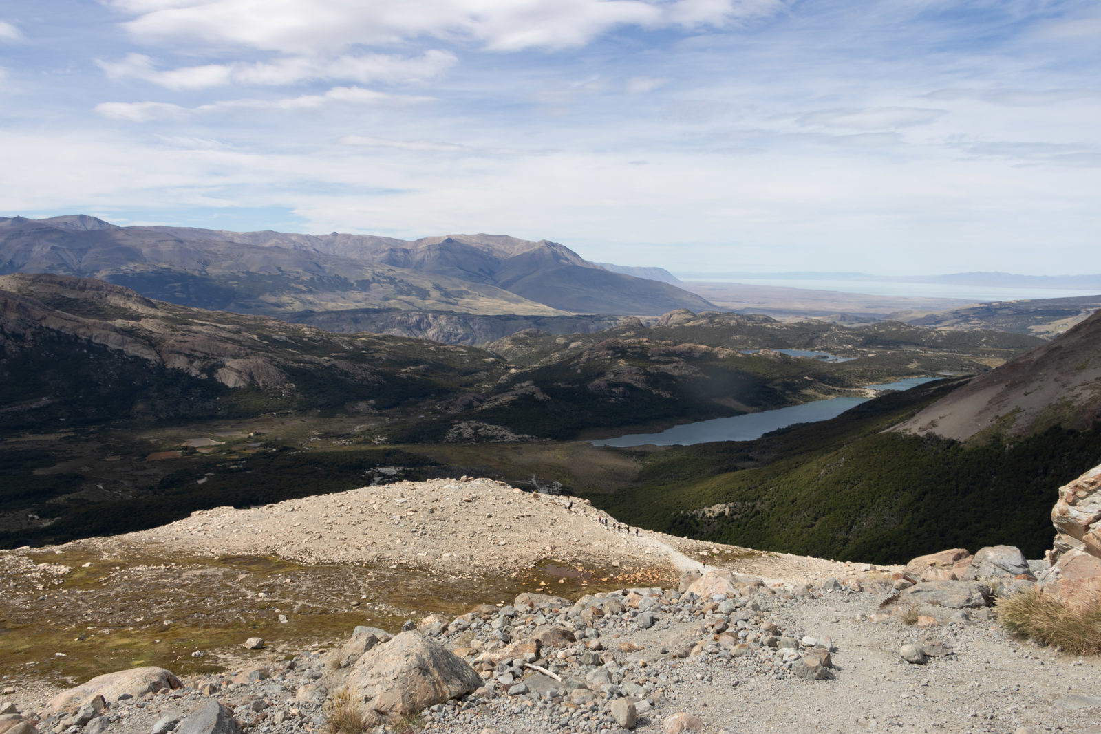 View back down the Laguna de los Tres trail towards Laguna Capri, with the rocky final climb in the foreground and Patagonian hills beyond.
