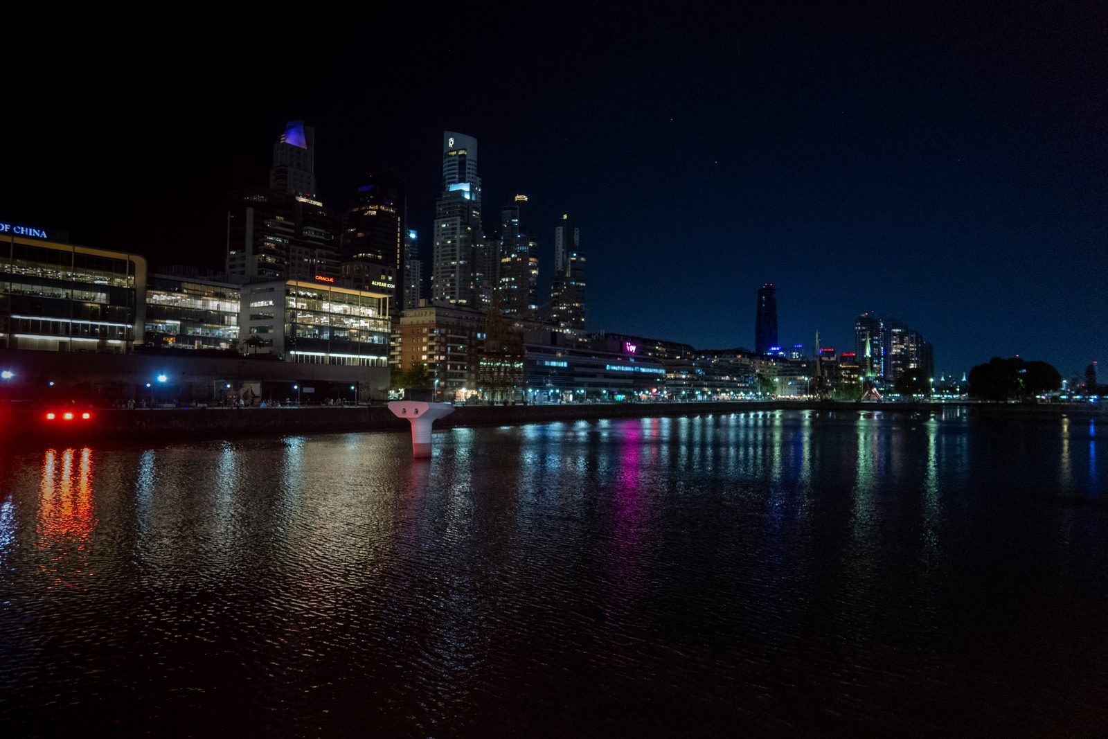 Night view of the Puerto Madero skyline in Buenos Aires, with illuminated modern buildings reflected in the waterfront.