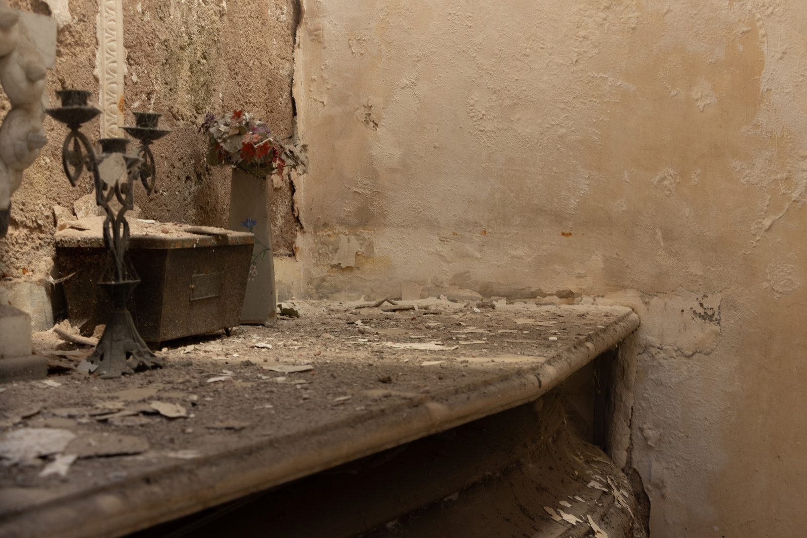 Dust-covered interior of an ageing family mausoleum in Recoleta Cemetery, Buenos Aires, showing worn stonework, candle holders and the effects of time.