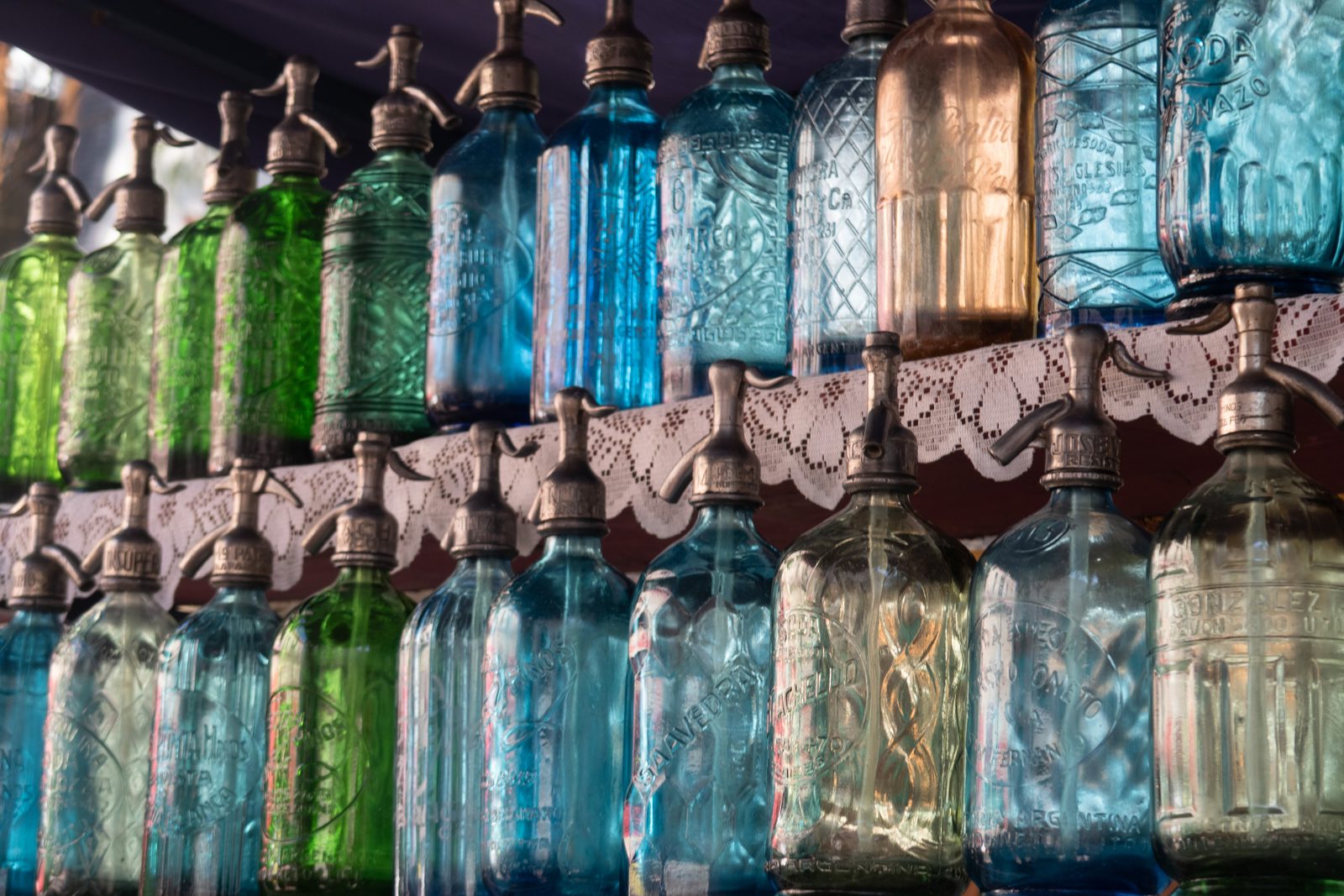 Collection of vintage coloured glass siphon bottles displayed for sale inside Mercado de San Telmo, Buenos Aires.