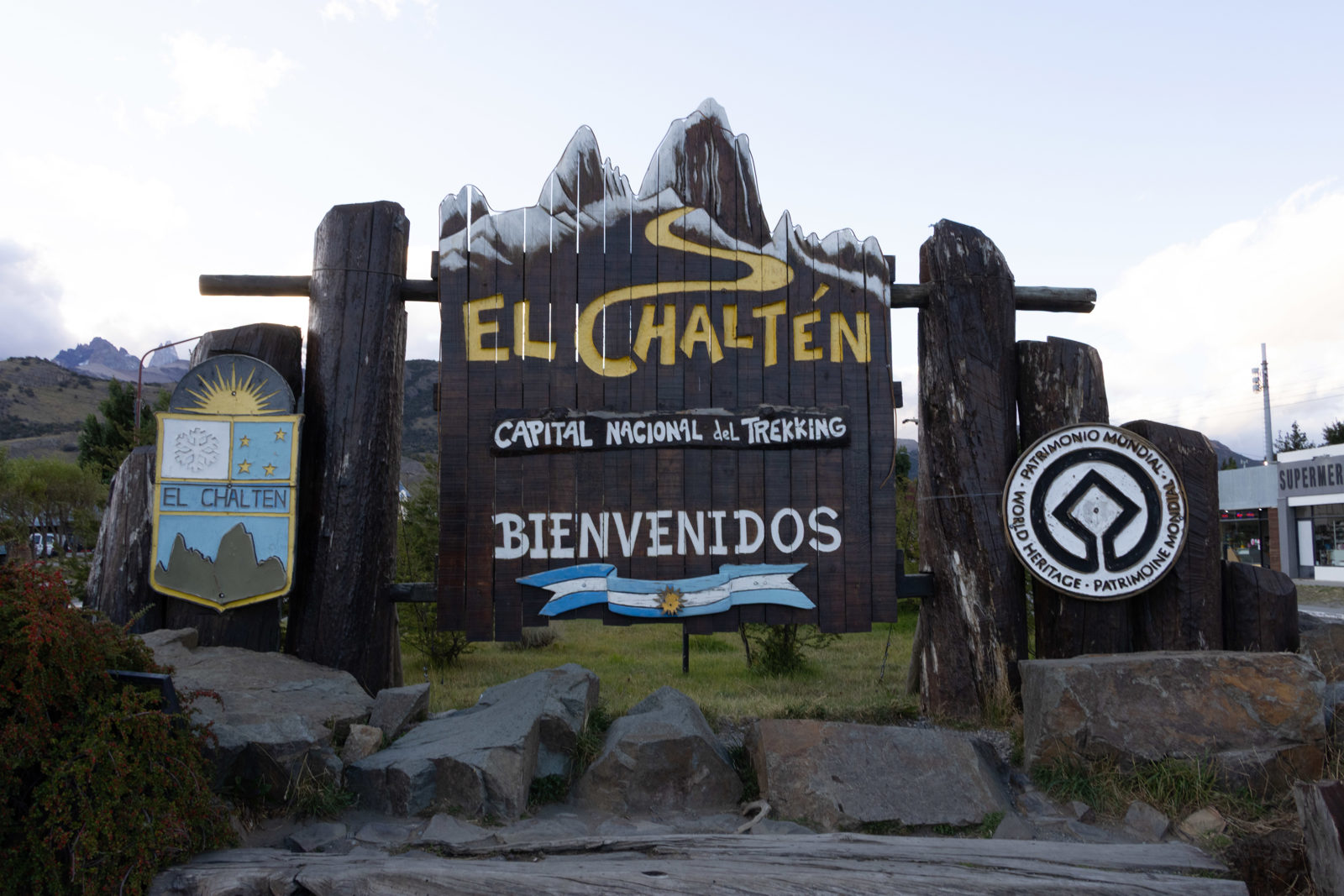 Welcome sign for El Chaltén, Argentina, with painted mountain peaks and trekking symbols.