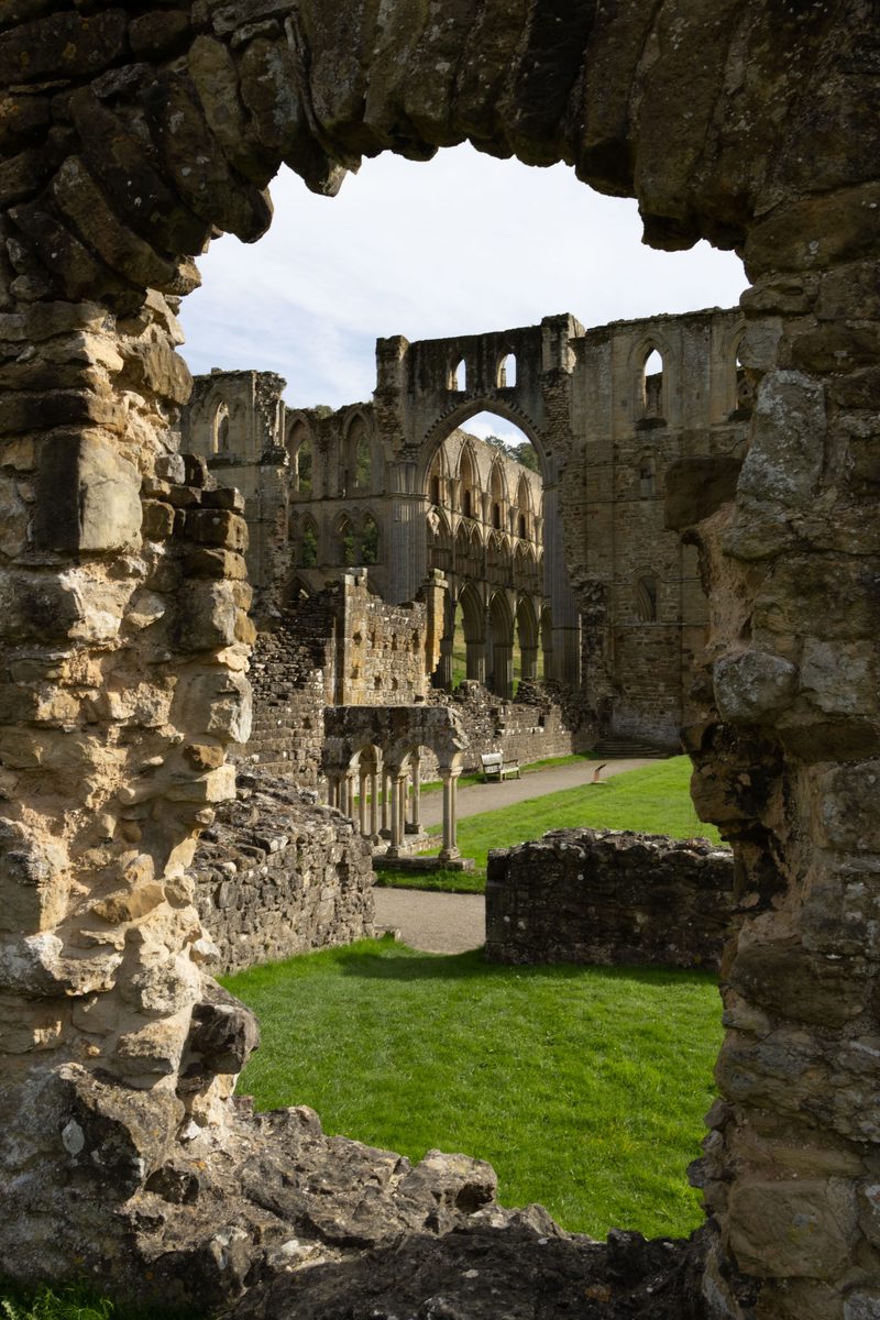 View of Rievaulx Abbey ruins through a rough stone opening