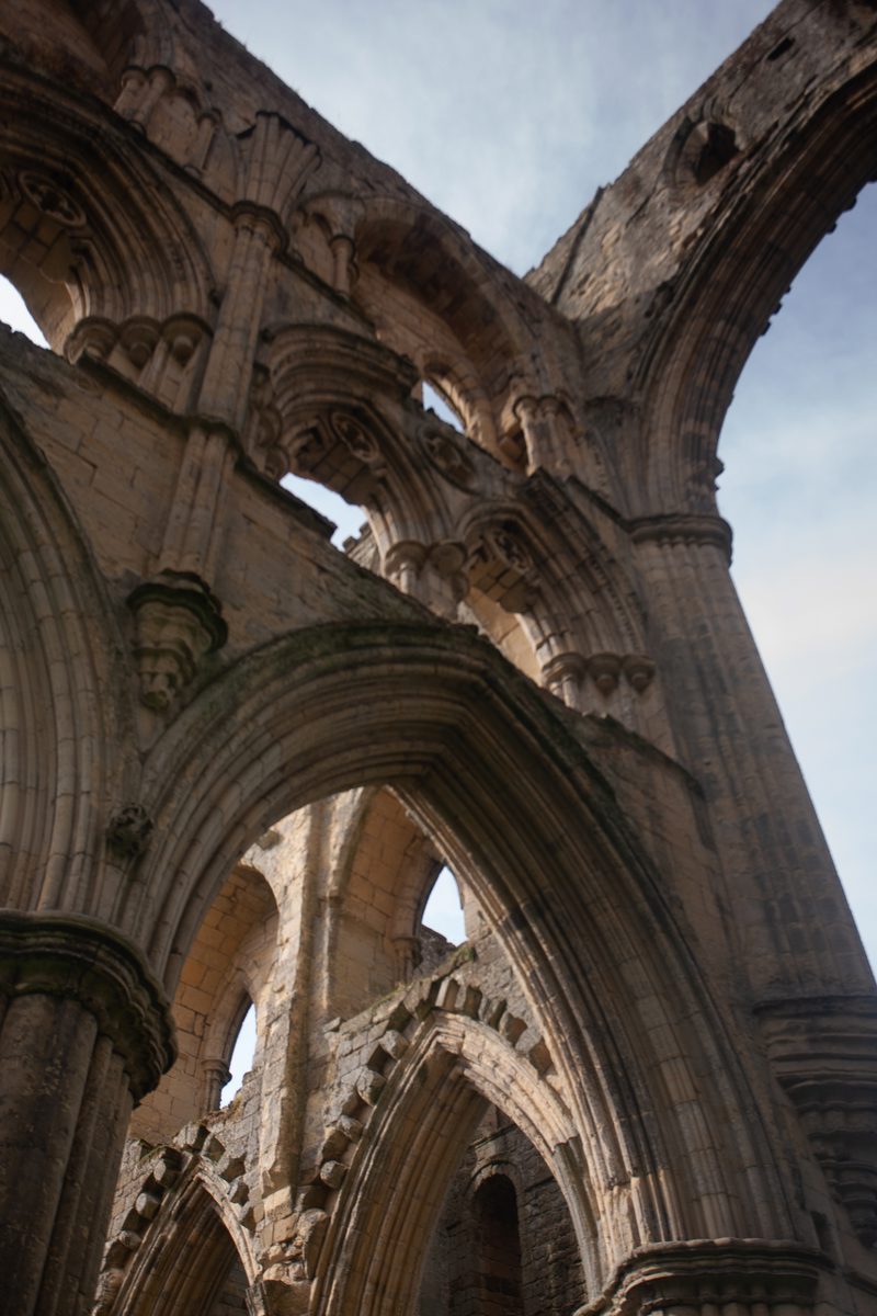 Upward view through intersecting stone arches at Rievaulx Abbey